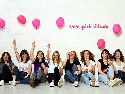 Bild der Pink Kids, die auf dem Boden sitzen und pinke Luftballons in der Hand halten